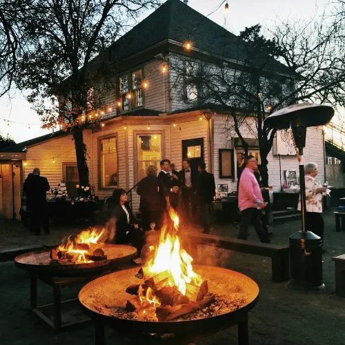 Outdoor holiday gathering with guests mingling around fire pits and a warmly lit house, emphasizing community and festive atmosphere for catering events in Pittsburgh.